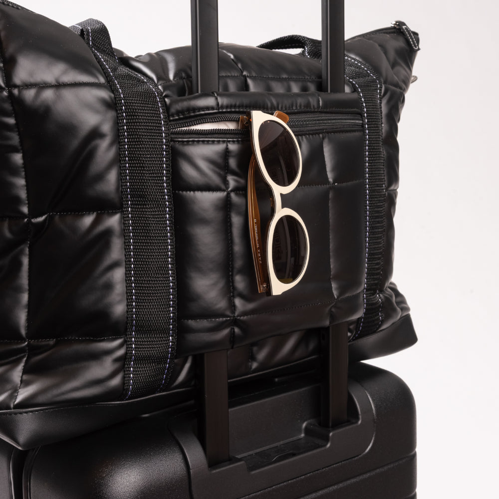 Black quilted duffel bag with sunglasses on a white background
