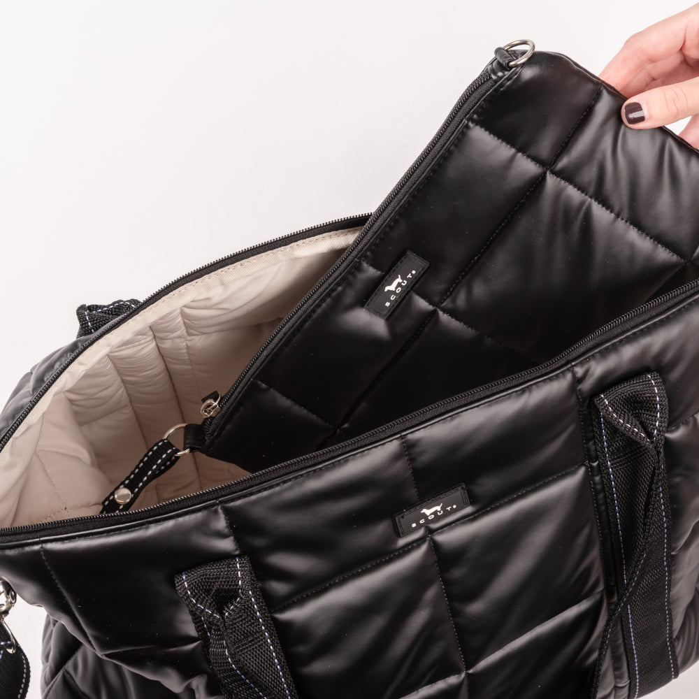 Black quilted bag with a hand opening it on a light gray background