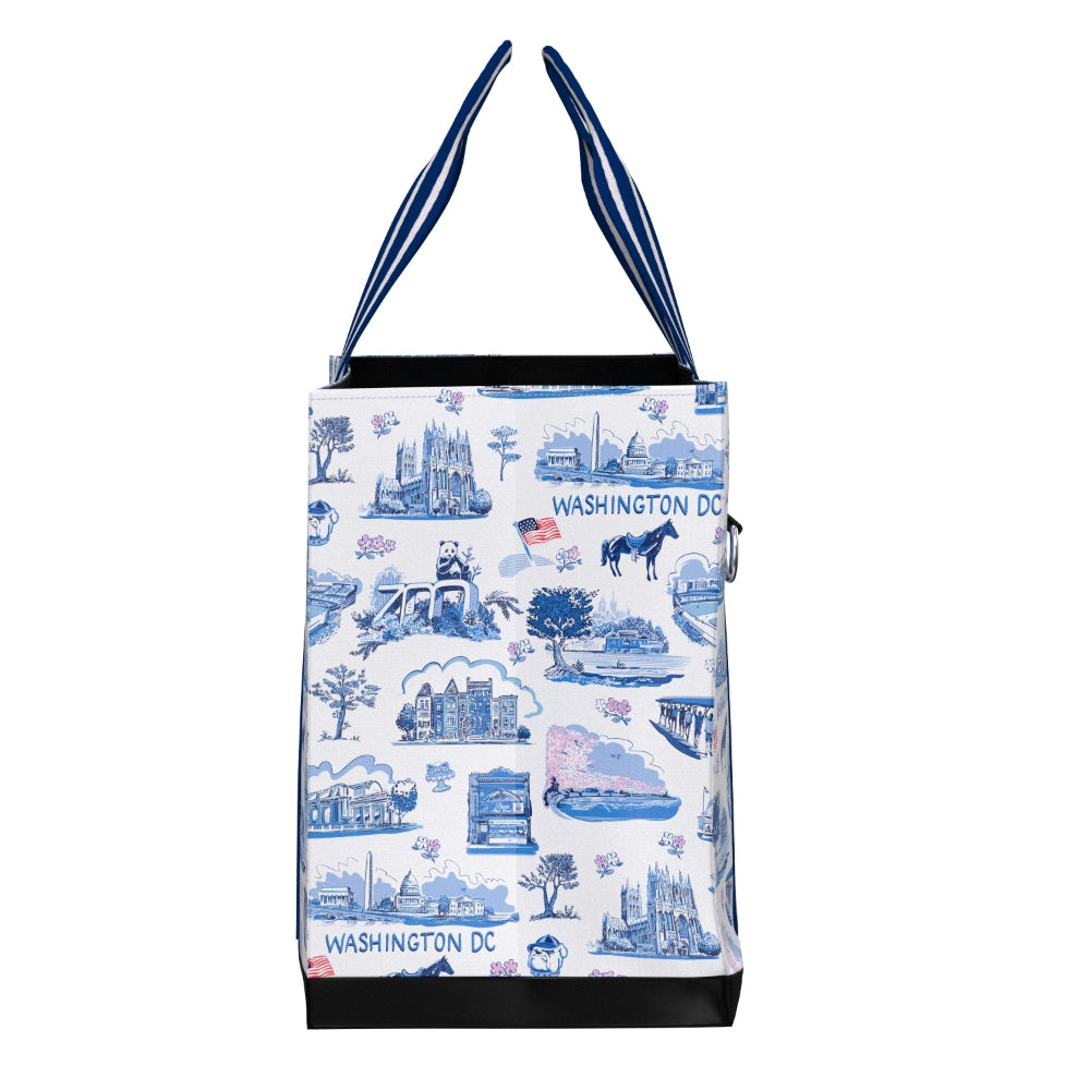 A white tote bag with a blue and pink Washington DC themed toile-style print, featuring blue and white striped shoulder straps and black trim at the base.