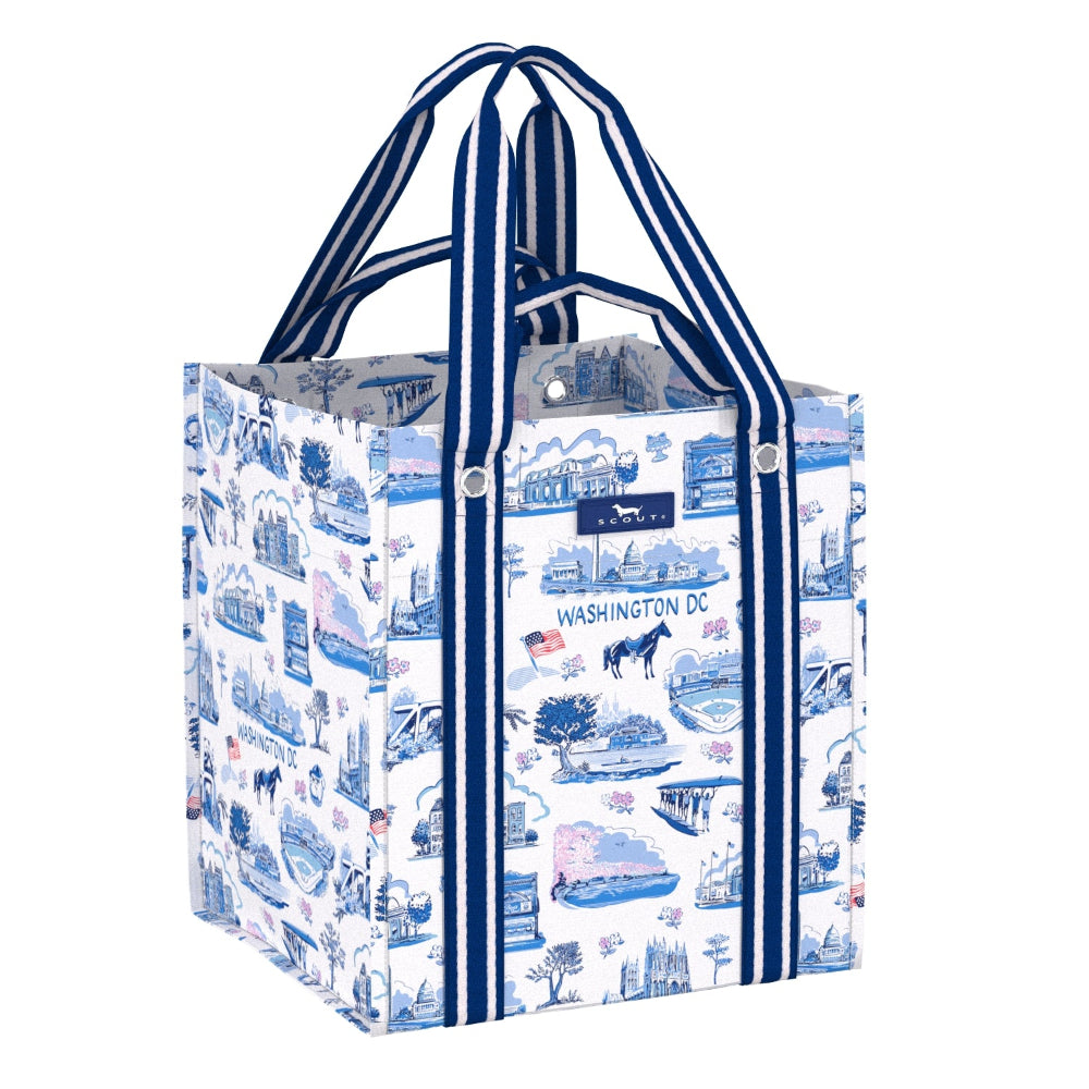 A reusable tote bag featuring a blue and white illustrated pattern of Washington DC landmarks and scenes, with navy blue and white striped handles.