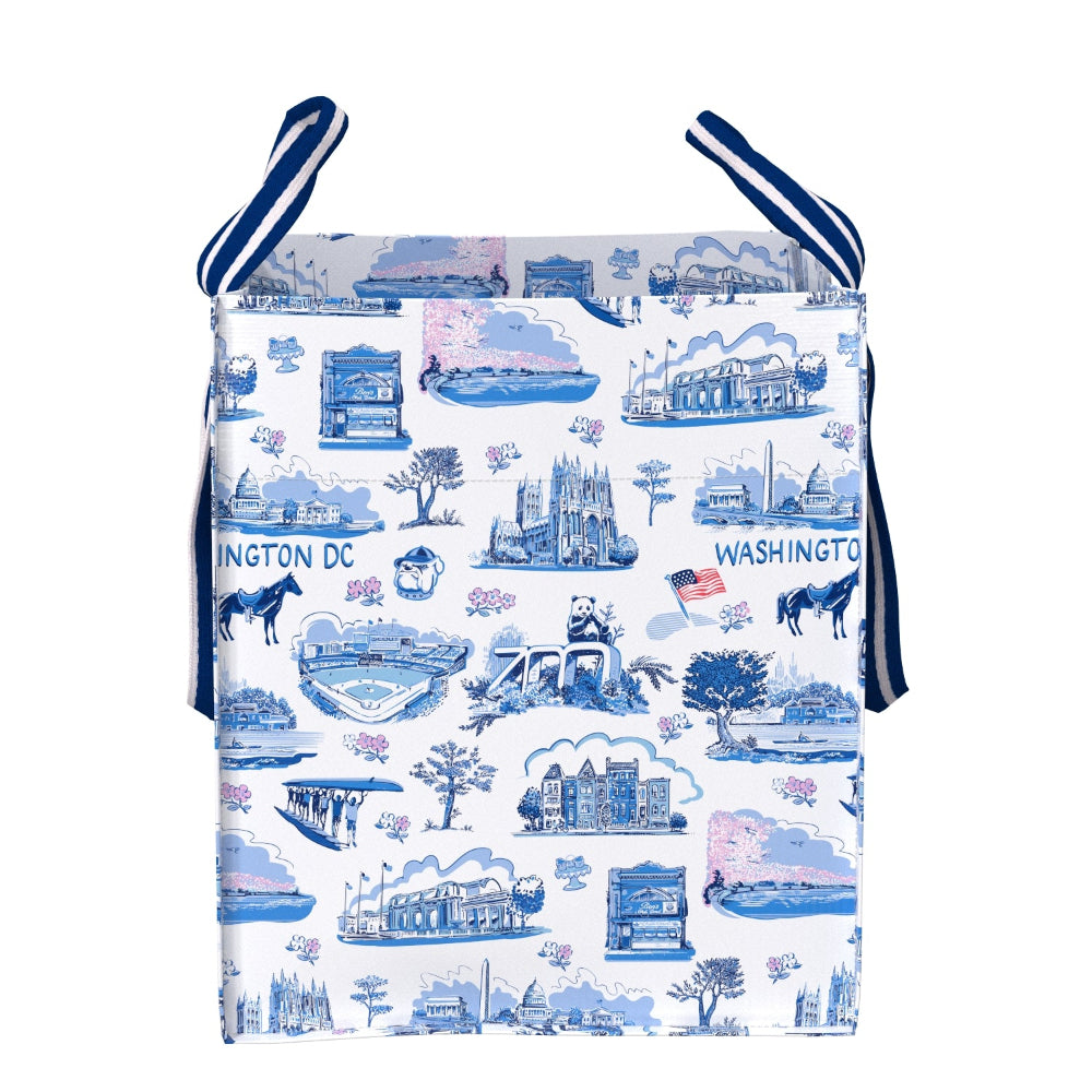 A fabric tote bag featuring a blue and pink illustrated pattern of Washington DC landmarks on a white background, with navy blue and white striped shoulder straps.