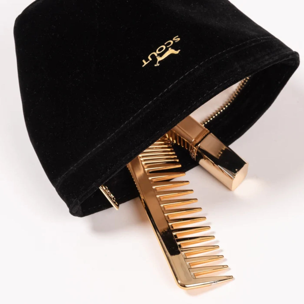 A black velvet cosmetic pouch with gold hardware, featuring a gold embroidered 'scout' logo and a gold comb-like zipper pull, shown on a white background.