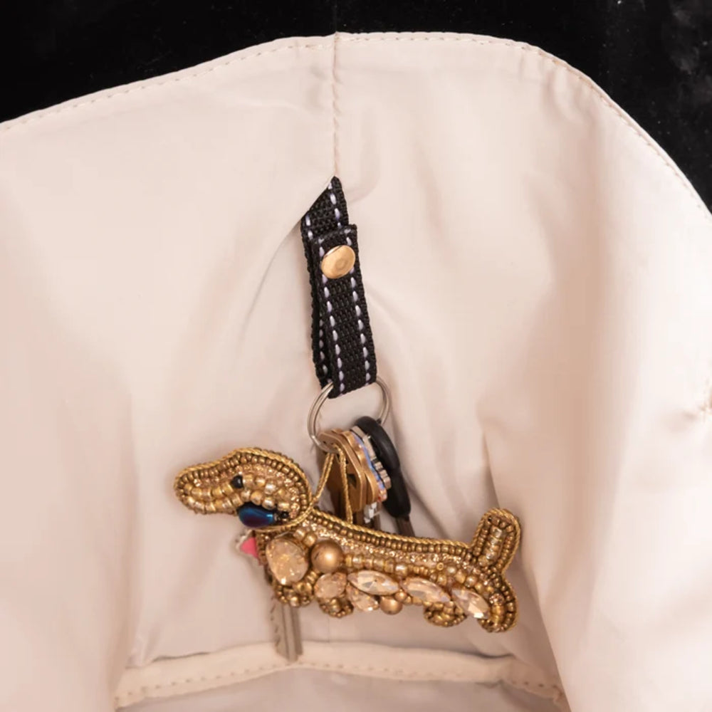 A close-up of the interior of a black velvet bag with beige fabric, black strap and a decorative gold-tone dachshund-shaped charm embellished with rhinestones and beads.