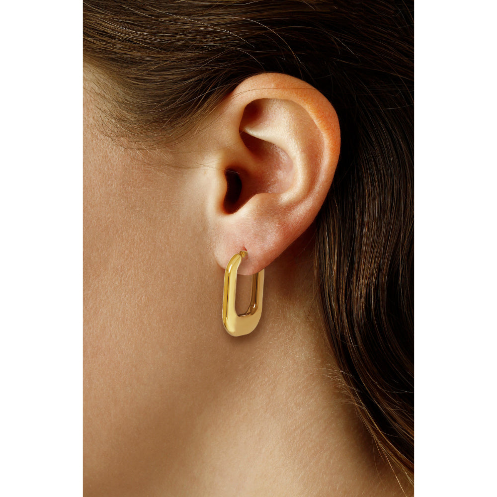 Gold earring worn on a person's ear with a neutral background