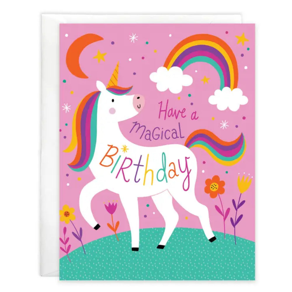 A colorful unicorn birthday card with a white envelope behind it. The card features a white unicorn with a rainbow mane and tail, a crescent moon, stars, clouds, flowers, and the text 'Have a magical Birthday' on a pink background.