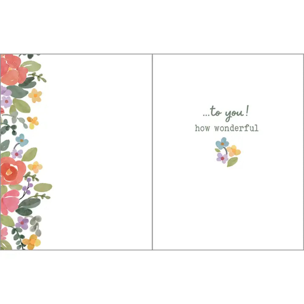 A greeting card shown open, with a floral border in coral, pink, green, yellow, and purple along the left side. The right panel contains the printed message “.
