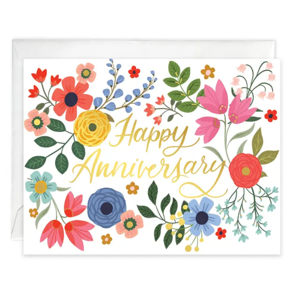 A floral anniversary greeting card with the words 'Happy Anniversary' in gold script, surrounded by colorful illustrated flowers and green leaves, shown with a white envelope behind it on a white background.