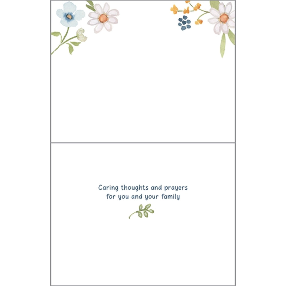 A folded greeting card shown front and back on a white background. The top panel has delicate watercolor-style flowers and greenery in the corners, and the bottom panel reads, 'Caring thoughts and prayers for you and your family' with a small green sprig below.