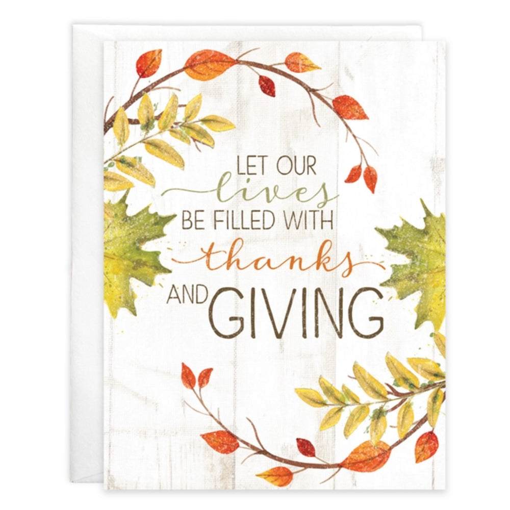 A greeting card with a white wood-textured background featuring autumn leaves in orange, yellow, and green, with the printed message 'LET OUR lives BE FILLED WITH thanks AND GIVING'.