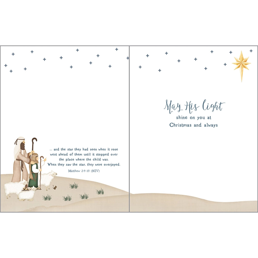 A split-panel Christmas greeting card design with a nativity scene on the left and a message on the right. The left panel shows a man, child, and sheep under a star in a desert setting.