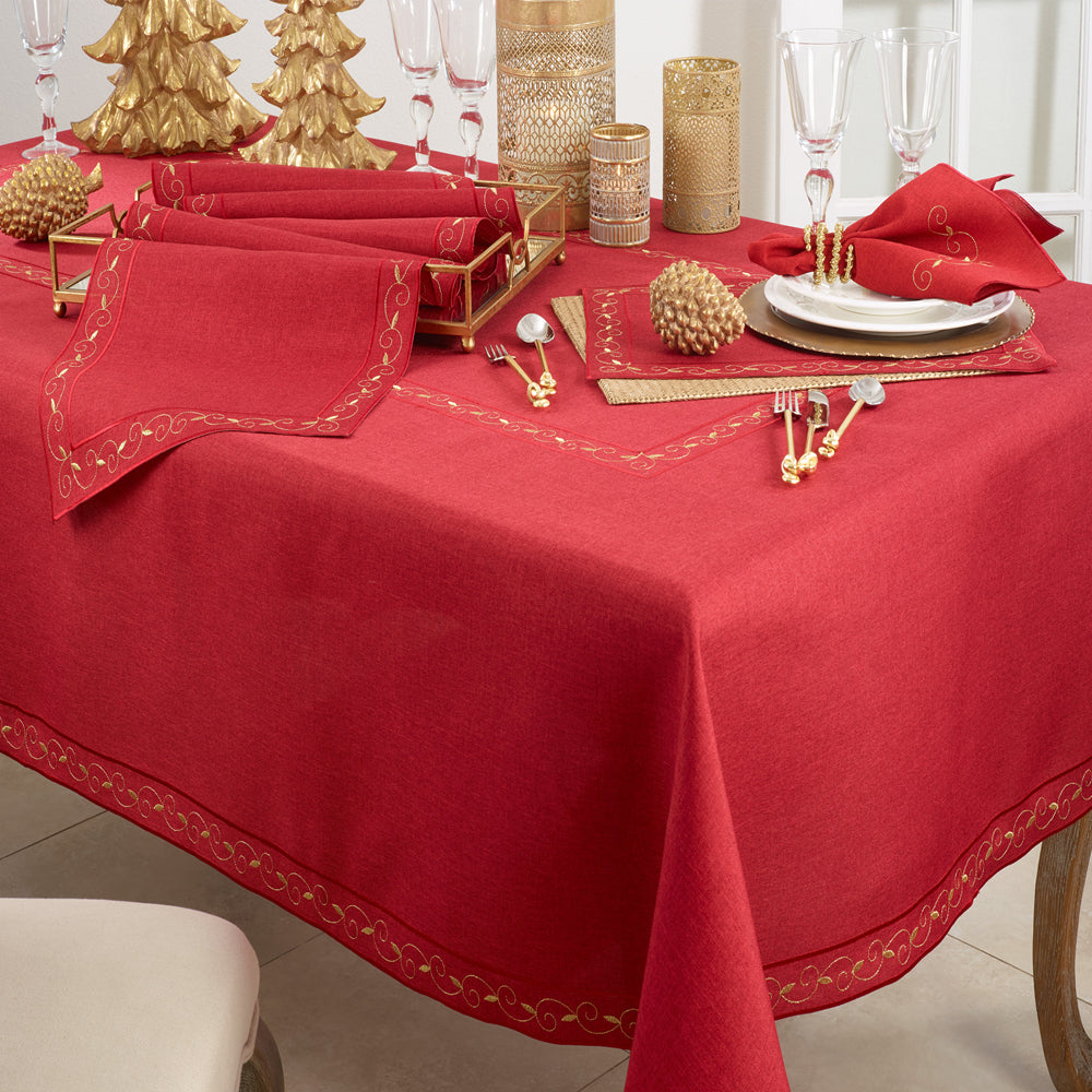 A red tablecloth with gold embroidered border details, styled on a dining table with gold-toned place settings, napkins, candle holders, and decorative elements.