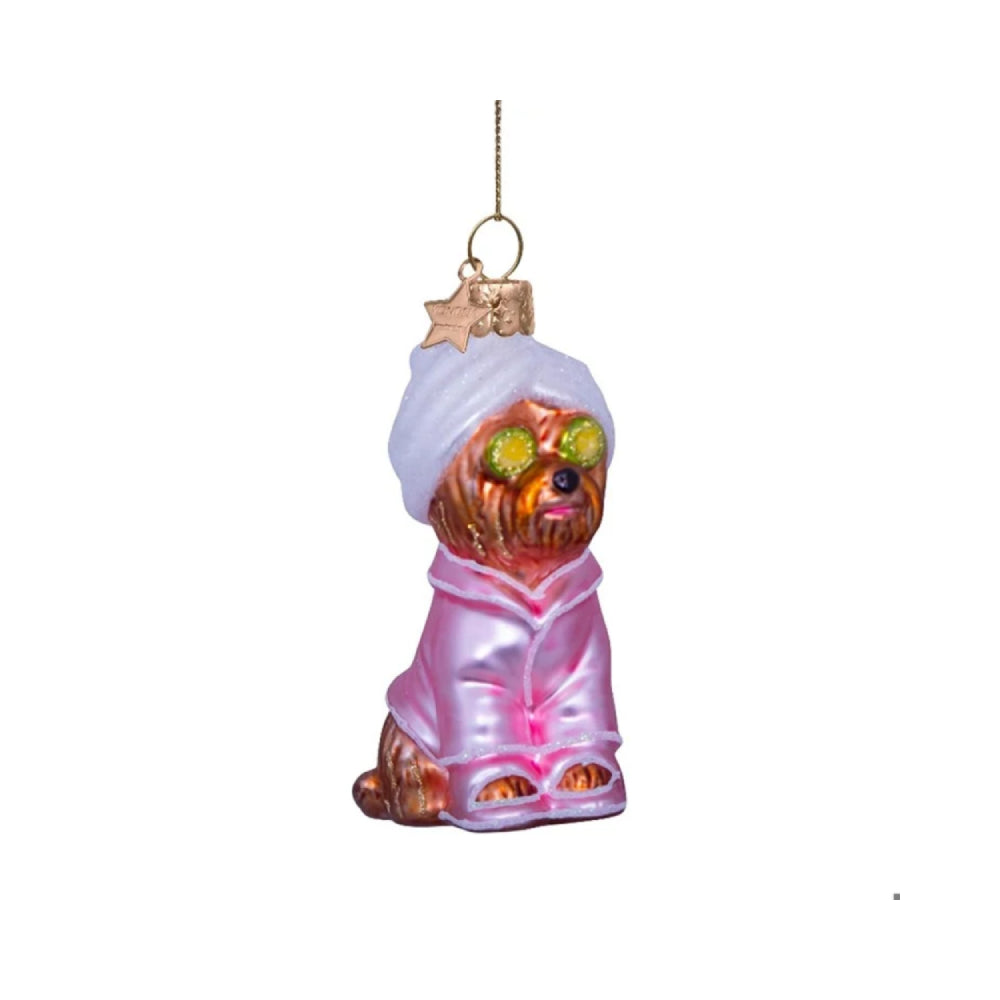 Glass ornament of a dog in a spa setting with a towel and robe on a white background