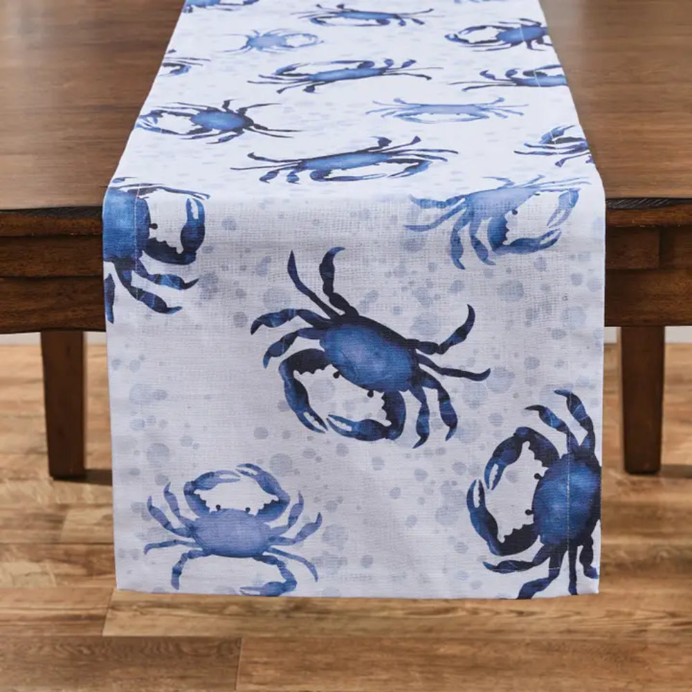 Table runner with blue crabs on white background displayed on wooden table. 