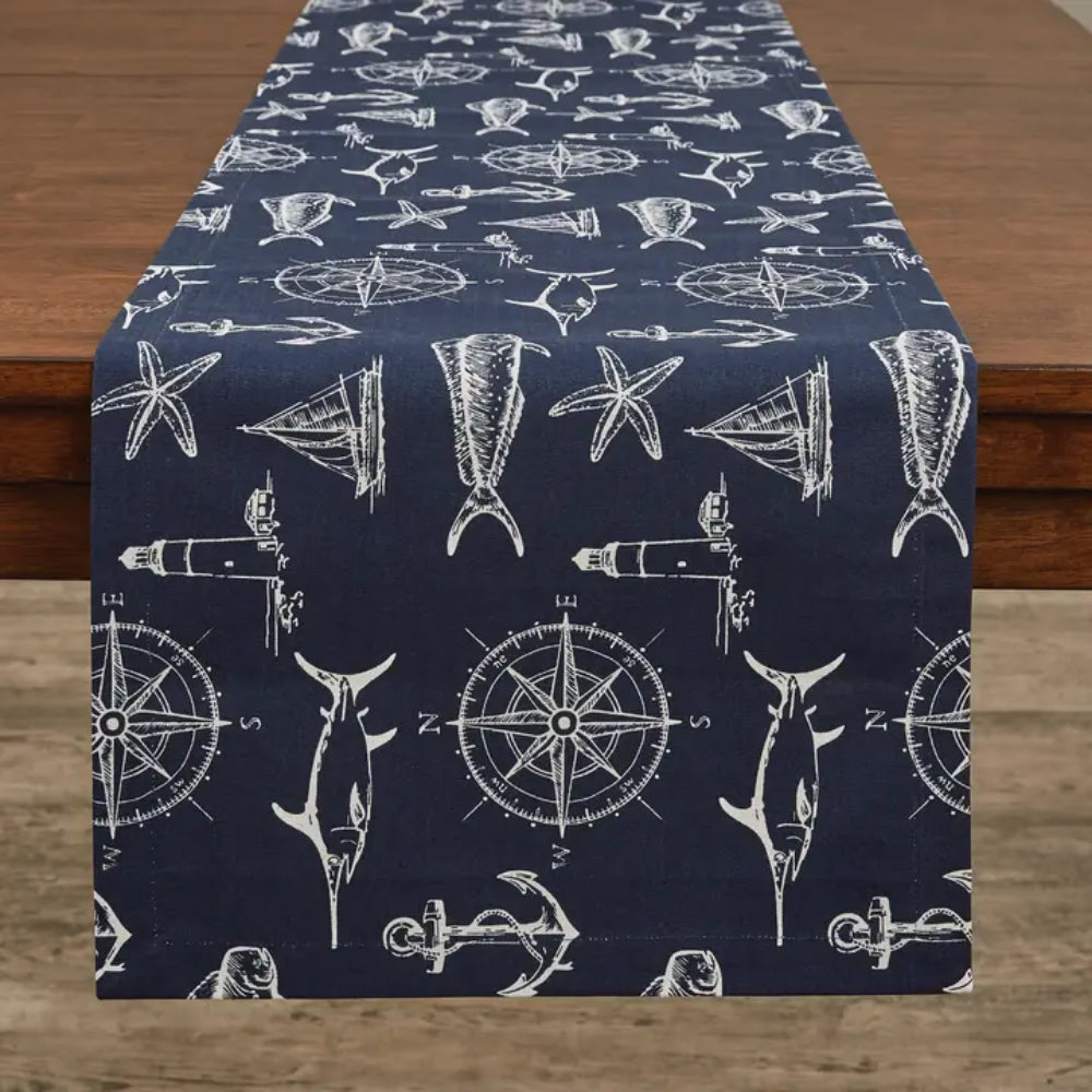 Navy table runner with Captain's Quarters theme with compasses, swordfishes, sails, and more designs on table runner on wooden surface. 