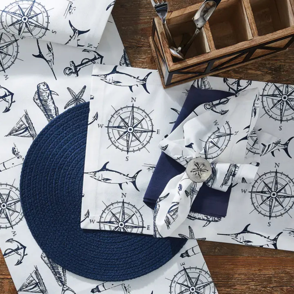 Captain's Quarters themed napkins, table runners with designs of compasses, swordfishes, anchors, and many more, displayed on wooden surface. 