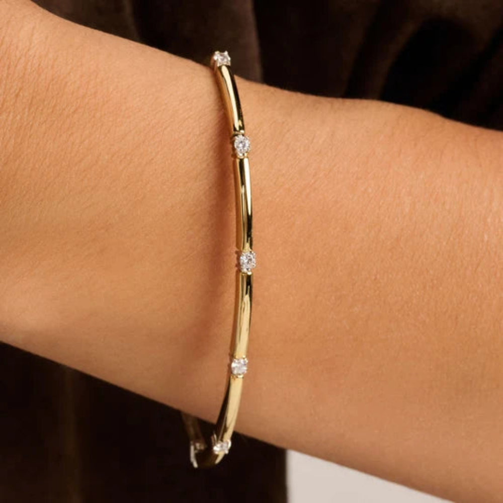 A close-up of a two tone gold bangle bracelet with small clear stones set along the band, worn on a person's wrist.