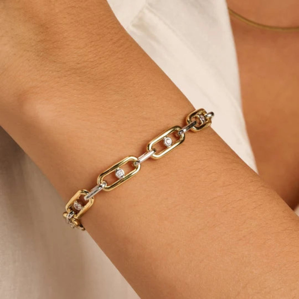 A close-up of a gold and silver chain bracelet with small clear stones, worn on a person's wrist.