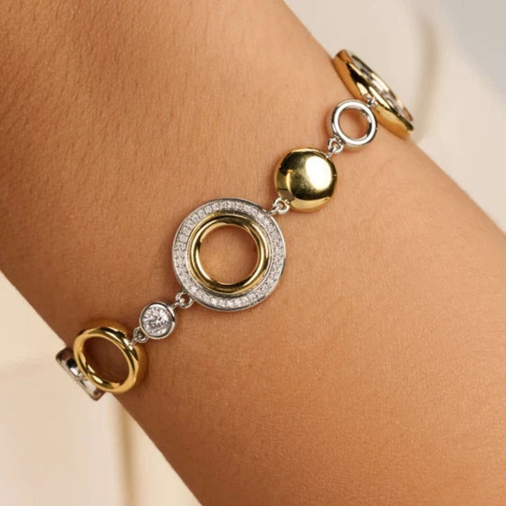 A close-up of a two-tone gold and silver bracelet with circular and spherical charms, worn on a person's wrist.