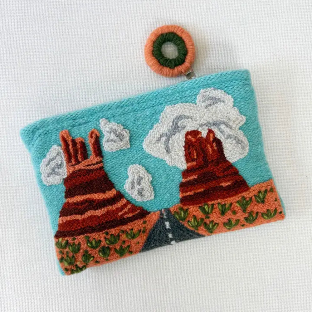 Handmade pouch with embroidered designs of mountains and clouds on a white background