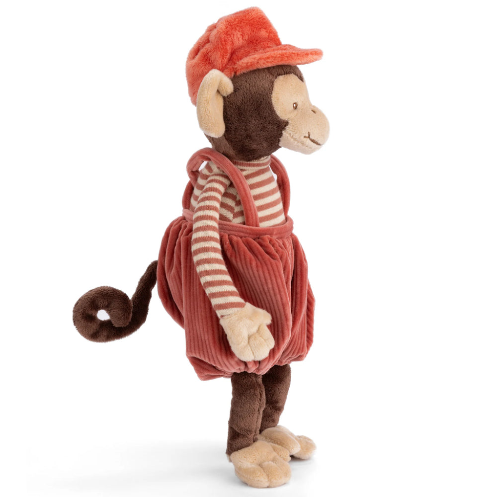 A side photo of a stuffed monkey toy wearing a red cap and overalls on a white background.