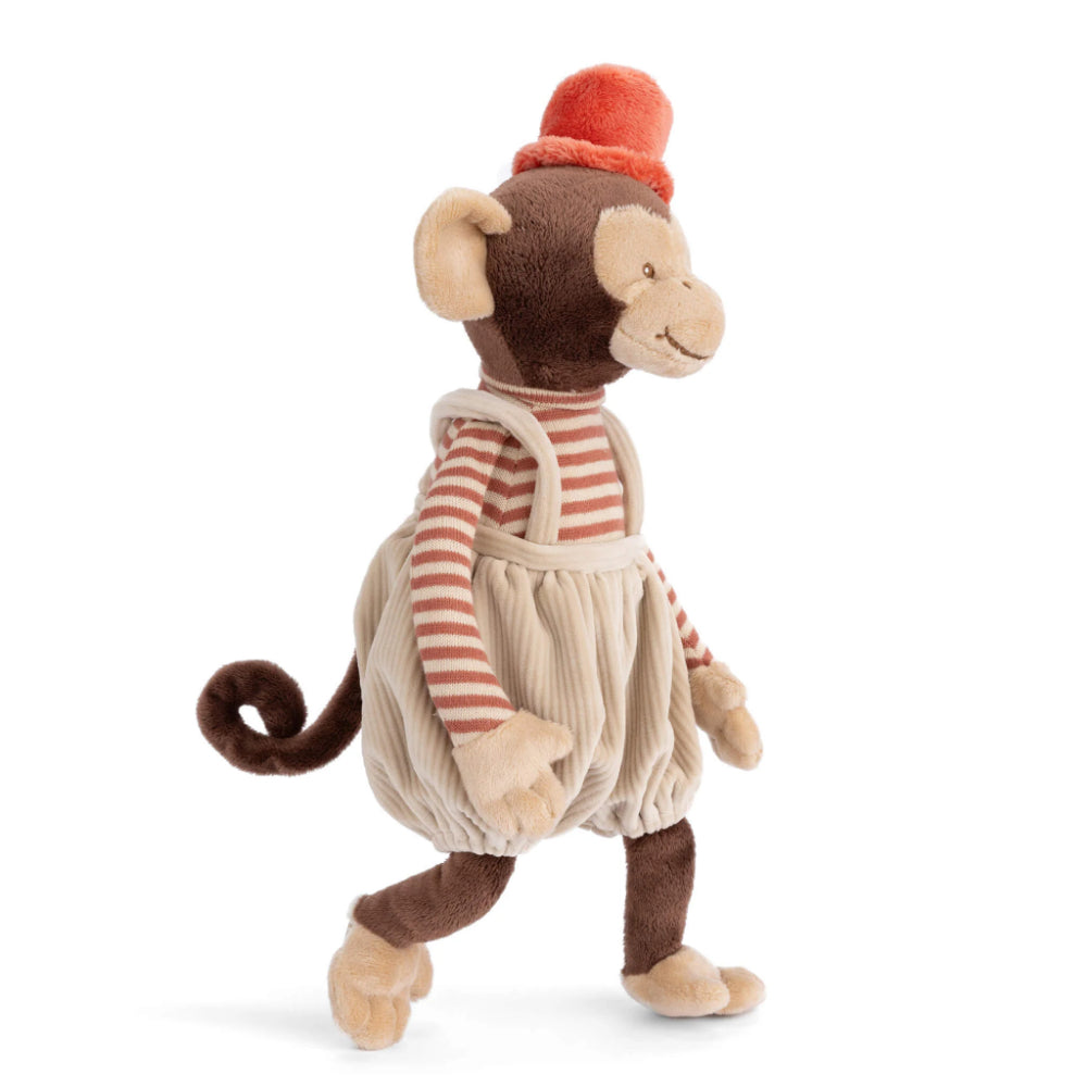 A photo of the side of a  tan stuffed monkey toy with a red hat and striped shirt and tan corduroy overalls on a white background. 
