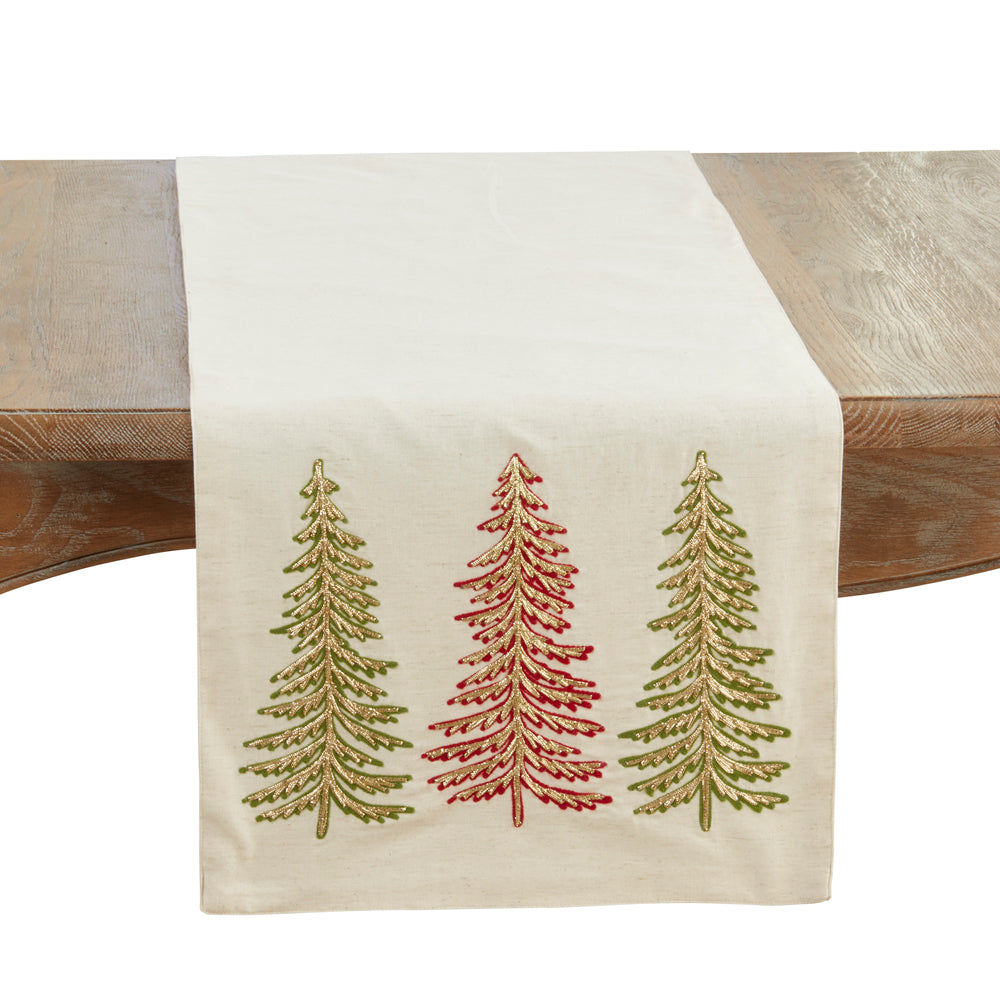 An off-white fabric table runner draped over a rustic wooden table, featuring three embroidered pine trees in olive green and red.