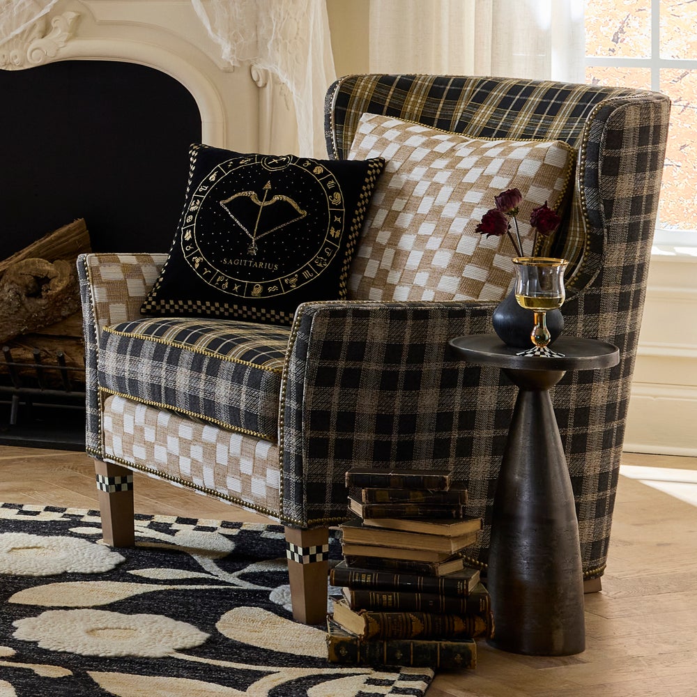 Plaid armchair with decorative pillows and a small table in a room with a fireplace.