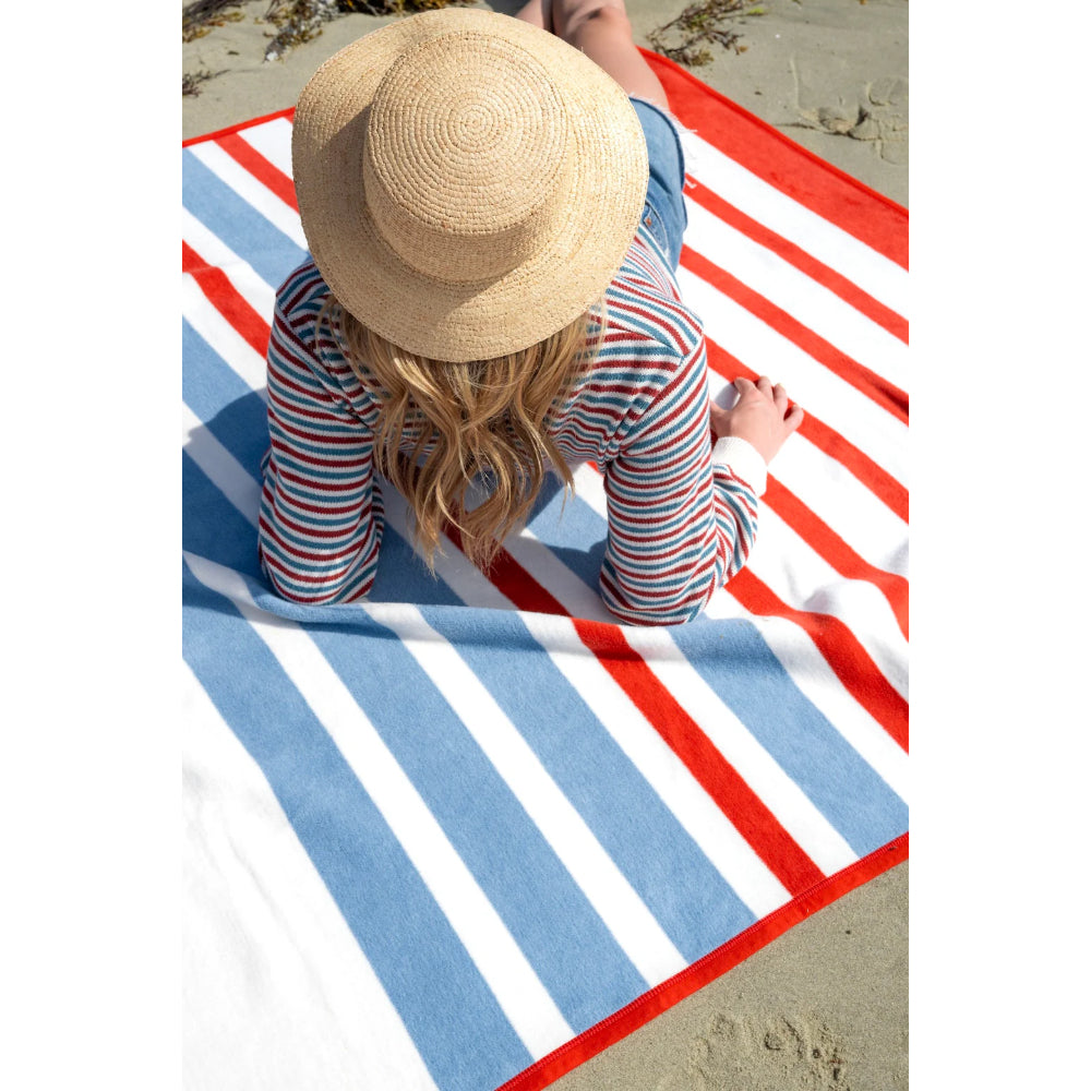 Person sitting on a striped blanket wearing a straw hat and colorful shirt.