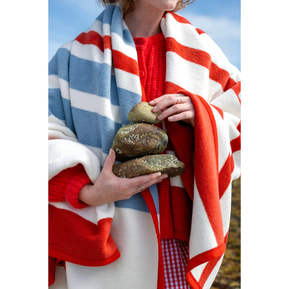 Person wrapped in a red, white, and blue striped blanket holding stones.