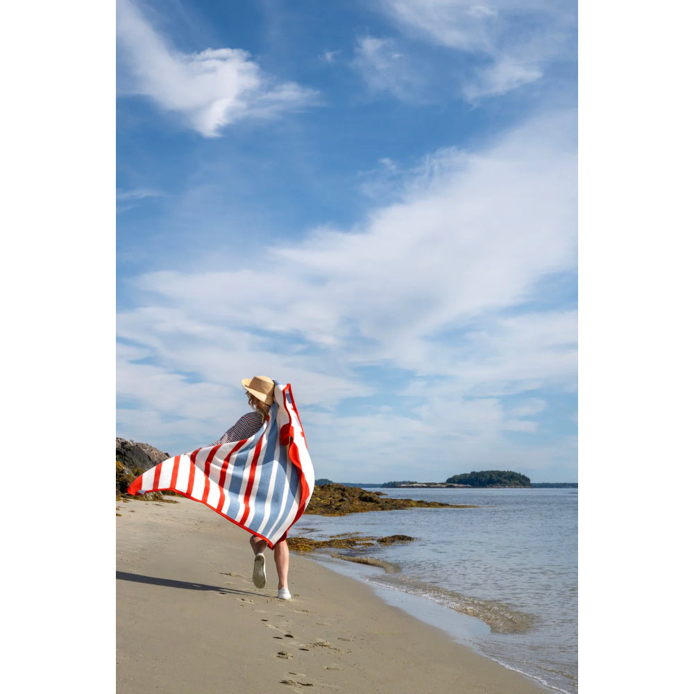 Person with a red and white striped blanket running on a beach with a blue sky.