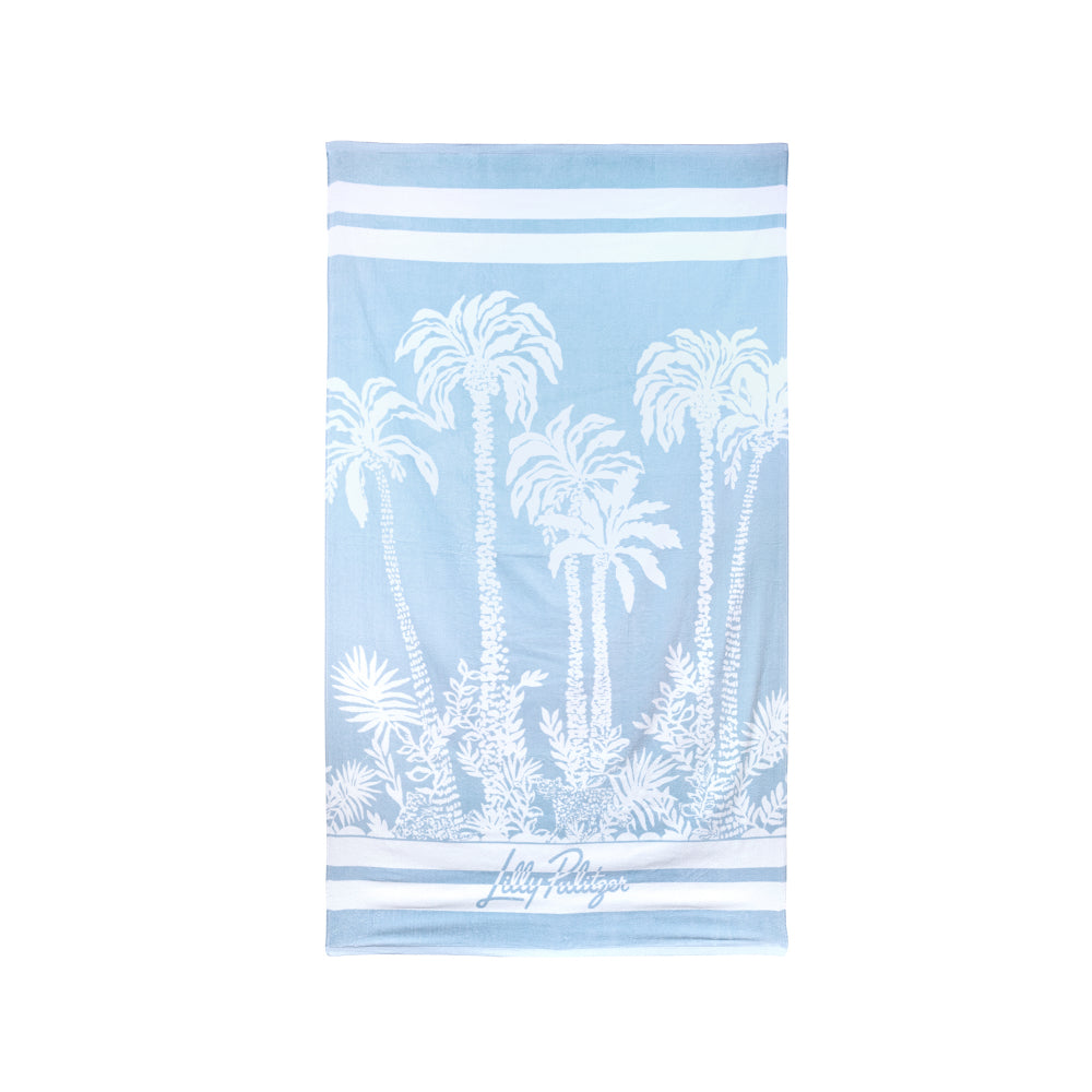 A light blue beach towel featuring a white palm tree and tropical foliage print, with white horizontal stripes at the top and bottom and a small 'Lilly Pulitzer' logo near the lower edge.