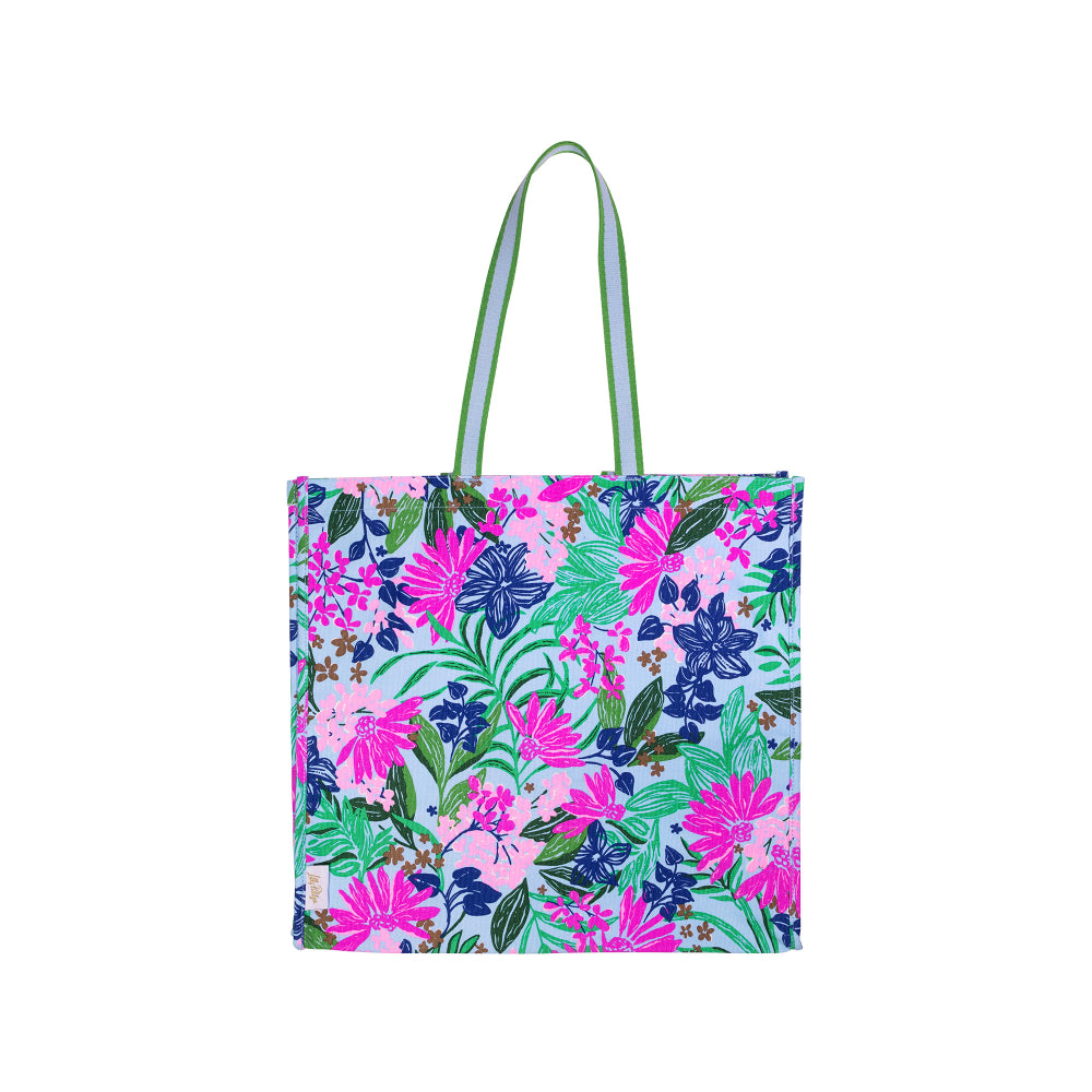 A tote bag with a vibrant tropical floral print in pink, blue, and green on a light blue background, featuring light green handles with white stripes.
