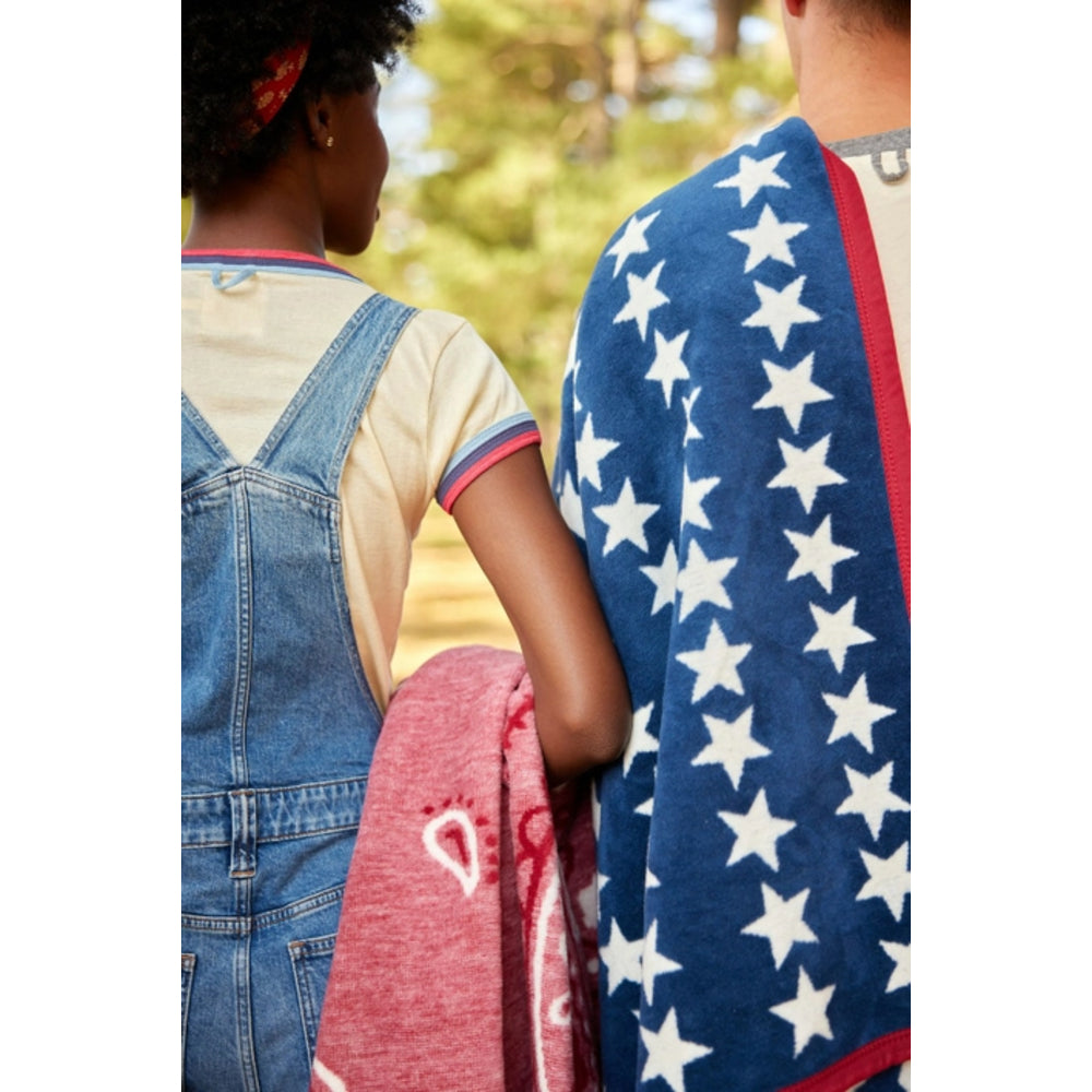 Two people standing close together, one wrapped in a red blanket and the other in a blue and white star-patterned blanket.