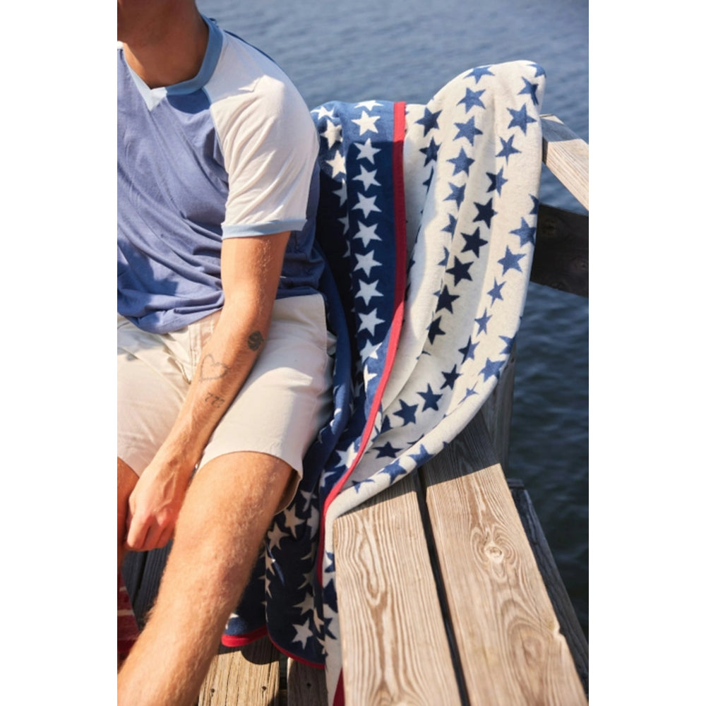 Person sitting on a dock with a star-patterned towel draped over their legs, water in the background