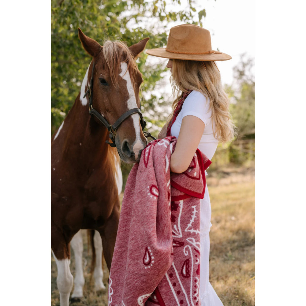 Woman in a white dress and brown hat standing next to a horse, holding a red patterned blanket