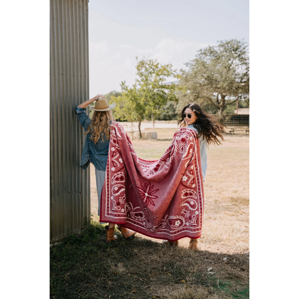 Two women with a red patterned blanket outdoors.