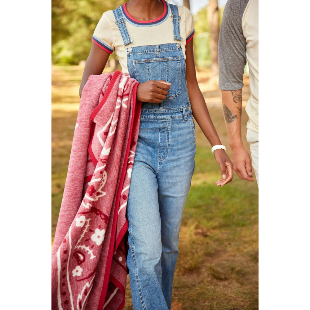 Person wearing denim overalls holding a red patterned blanket outdoors