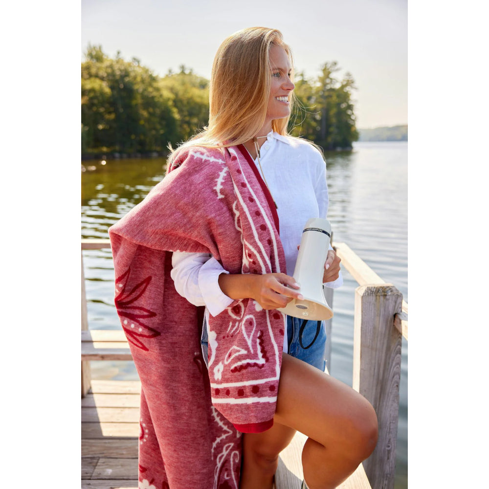 Woman standing by a lake, wearing a red patterned cover-up and holding a whitesound device. 