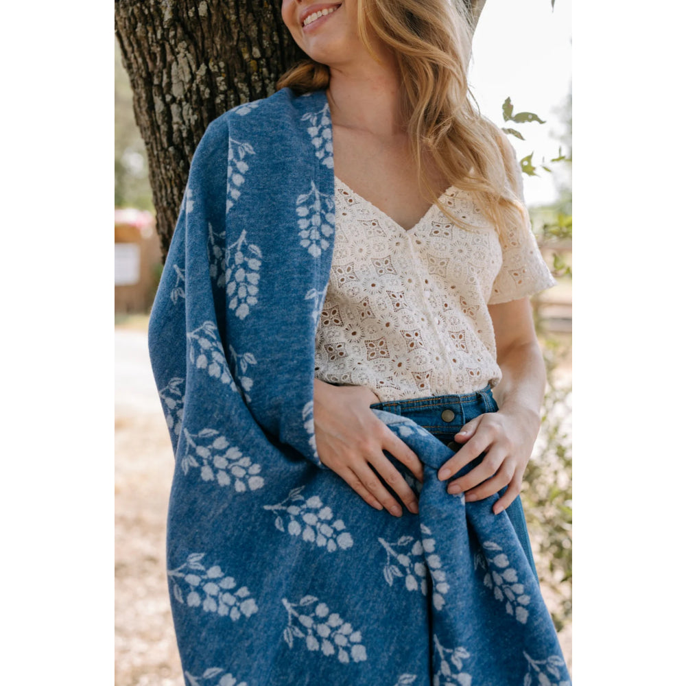 A woman holding a lightweight blanket with blue colors and white flowers on it. 