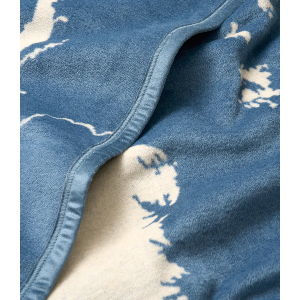 A close-up of a plush blue blanket with a white tie-dye or brushstroke pattern and a stitched border.