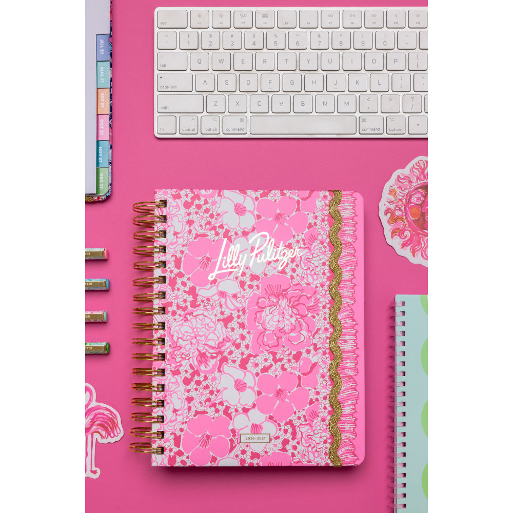 Floral notebook with 'Lilly Pulitzer' branding on a pink desk with keyboard and stationery.