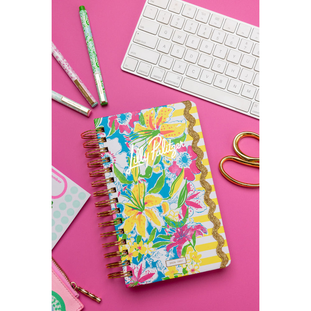 Colorful notebook with floral design on a pink surface with stationery items.