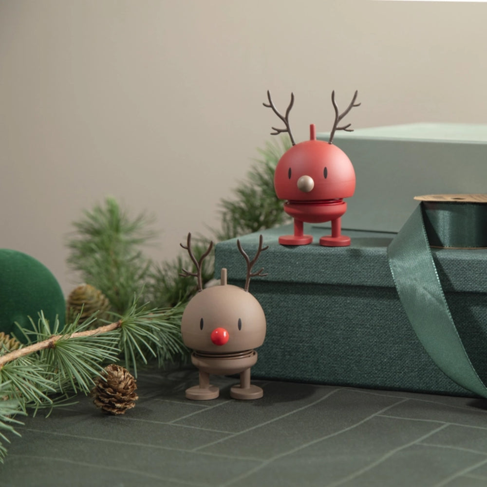 Two small holiday reindeer figurines styled on a dark green gift box with pine branches and a ribbon in the background.
