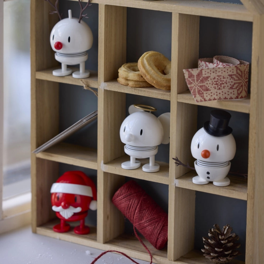 A light natural wood 12-compartment cube shelf organizer styled with holiday decorations, including a white reindeer, a white snowman with a black hat, a Santa Claus figurine, a red spool of thread, and a pinecone.