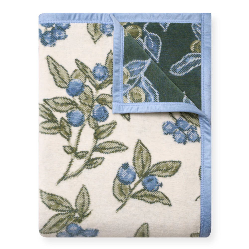 Floral patterned blanket with blueberries and green leaves on a white background