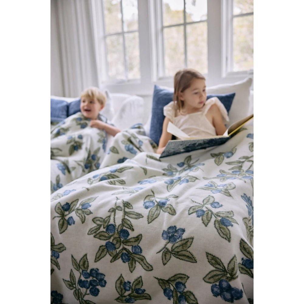 Two children on a bed with floral bedding in a bright room.
