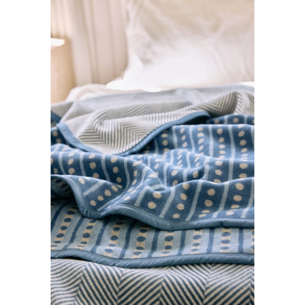 A close-up of a blue patterned blanket draped over a bed with white bedding in the background.