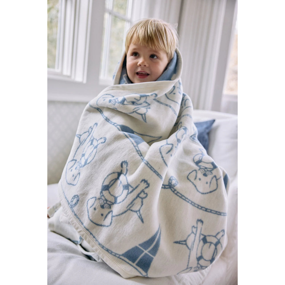 Child wrapped in a blanket with blue animal patterns in a bright room.