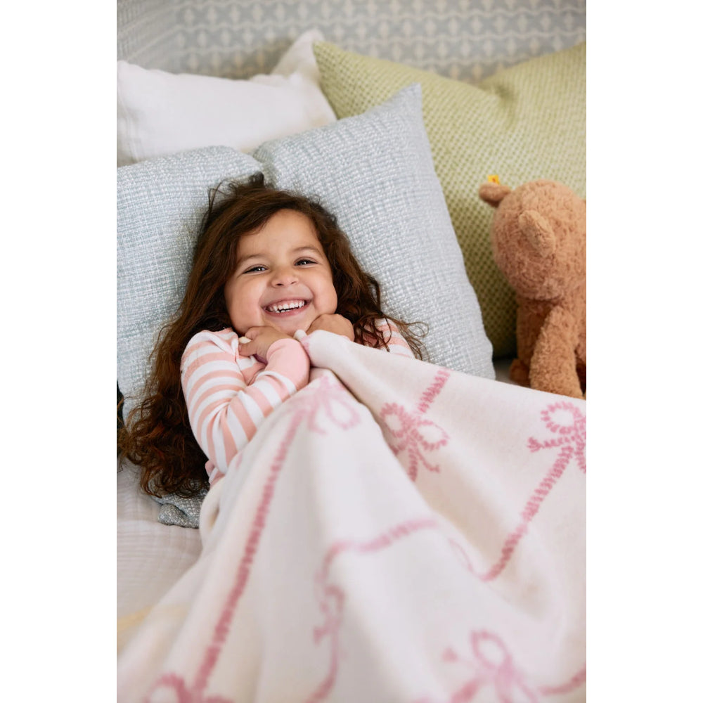 Child wrapped in a pink blanket with a teddy bear and pillows in the background