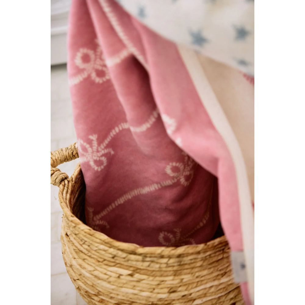 Pink fabric with white patterns draped over a woven basket on a light wooden floor.
